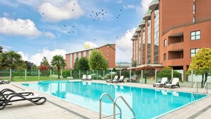 Una piscina con sillones de descanso, un edificio de hotel y un cielo despejado.