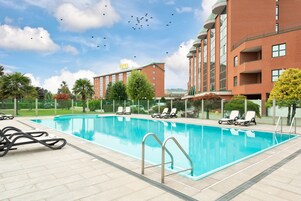 Piscina com espreguiçadeiras, um edifício de hotel e céu claro.