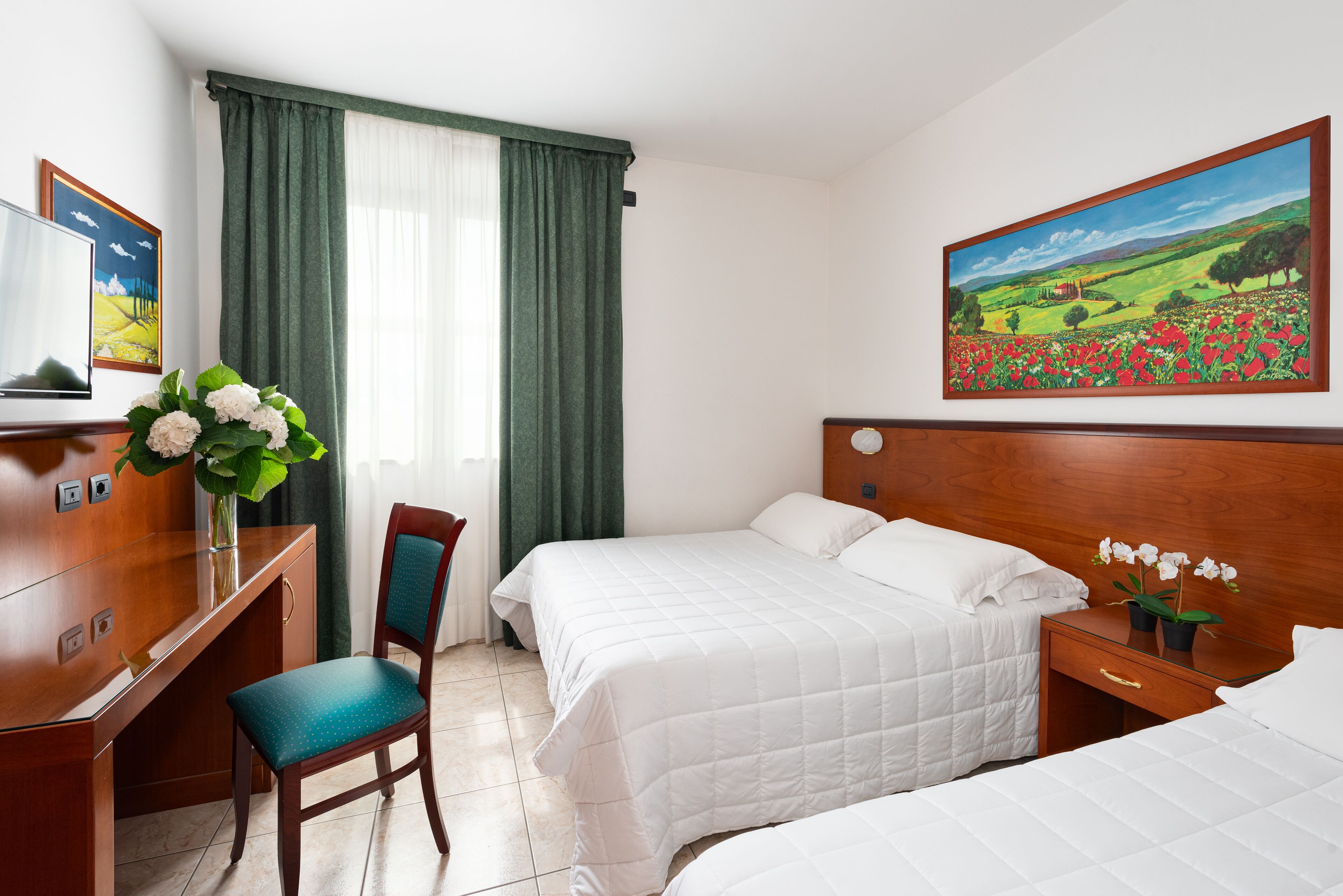 A hotel room with two beds, a desk, a chair, a TV, and a painting on the wall.