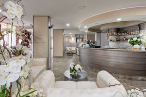 Uma área de bar moderna com balcão curvo, assentos de couro branco e um arranjo floral.