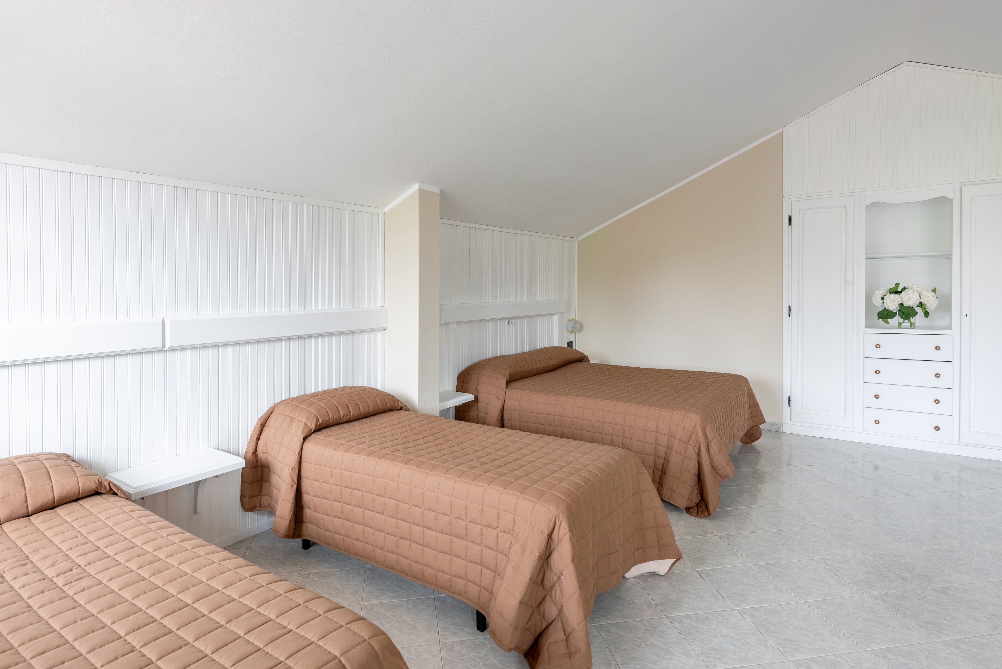 A bedroom with three beds, a white wardrobe, and a window.