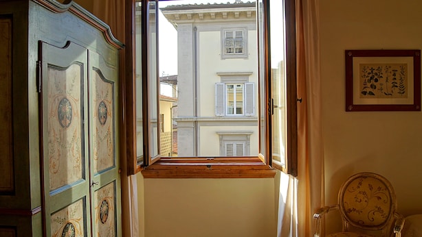 Ein Zimmer mit einem raumhohen Holzfenster, einem grünen Schrank mit aufwendiger Verzierung und einem Stuhl mit Blumenmuster.