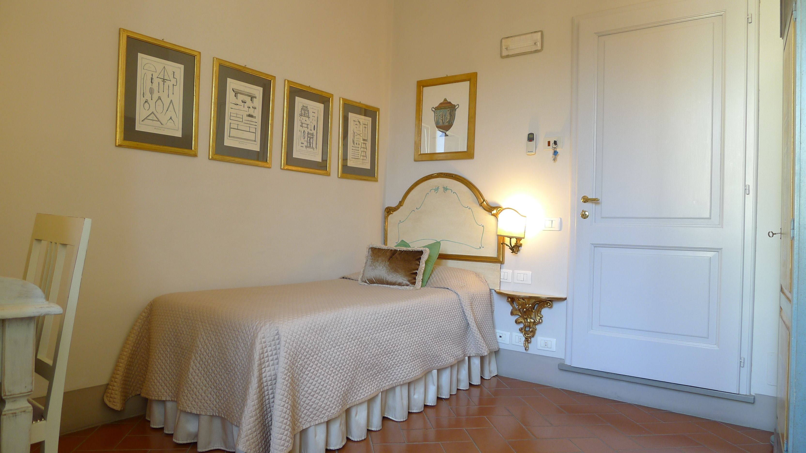 A bedroom with a bed, a chair, a door, and four framed architectural drawings on the wall.