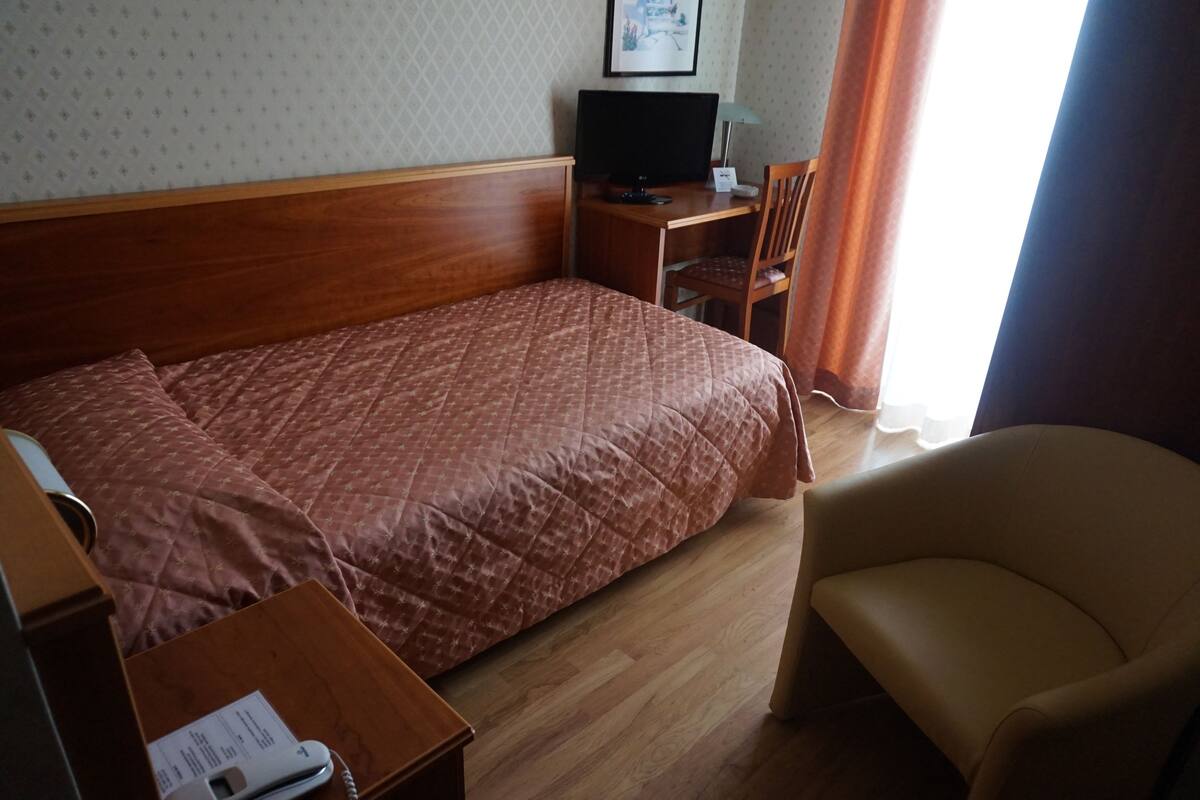 Una habitación de hotel con una cama, un escritorio con computadora, una silla y un teléfono.
