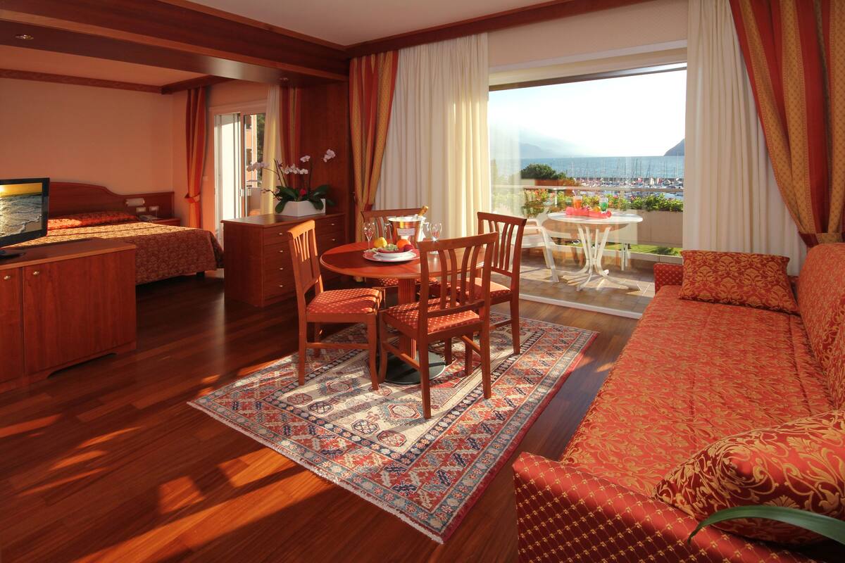 Una habitación de hotel con balcón, zona de comedor, sofá y televisor.