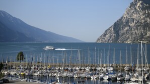 A marina with numerous boats docked, a large mountain in the background, and a clear blue sky. - Riviera (Riva del Garda)