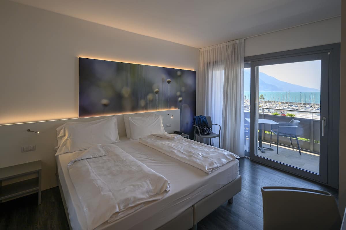 Habitación de hotel con una cama grande, una mesita de noche, una silla y vistas a un puerto deportivo.