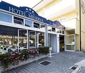 Un hotel llamado "Hotel Minerva" con un letrero de bar cafetería sobre la entrada.