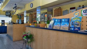 A reception desk with a clock, a blue signboard, and a mirror reflecting the interior. - Hotel Minerva (Lignano Sabbiadoro)