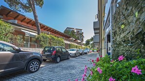 A row of parked cars along a cobblestone street, adjacent to a building with a stone facade and a balcony. - Hotel Minerva (Lignano Sabbiadoro)