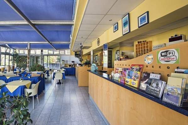 Un restaurante con mostrador de recepción, mesas, sillas y un toldo azul.