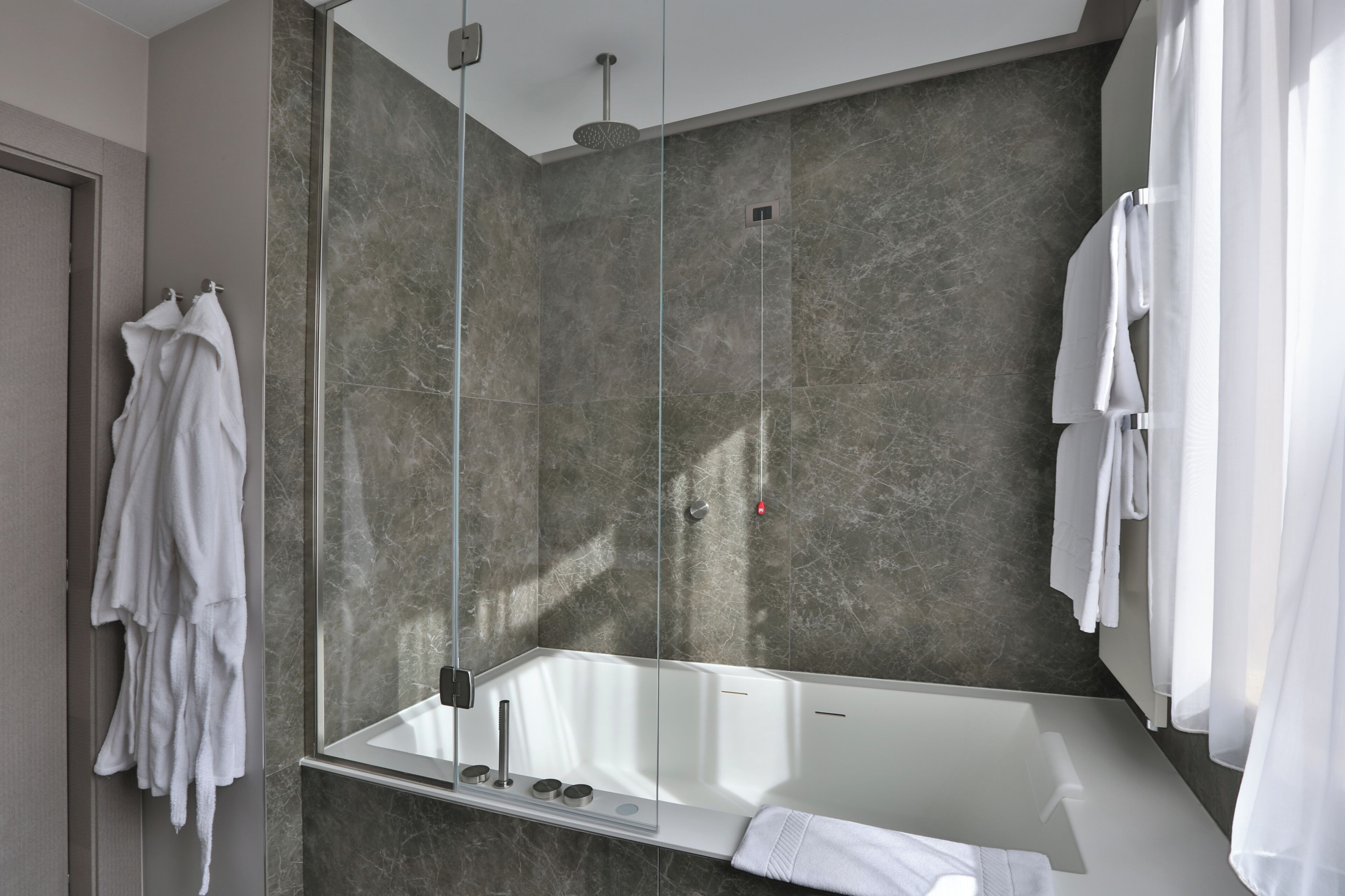 A modern bathroom with a glass-enclosed shower, a large mirror, and a white bathtub.