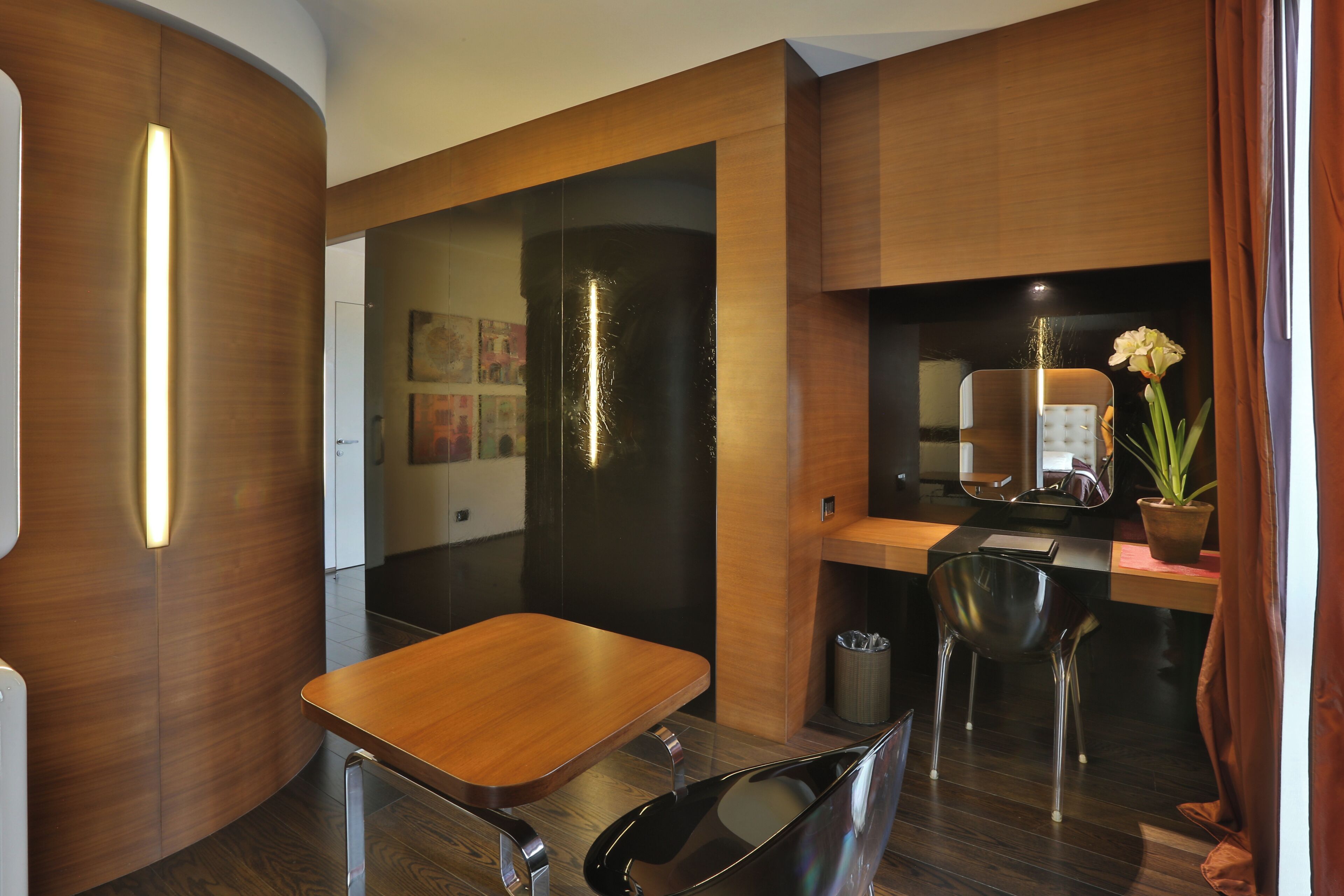 Habitación de hotel moderna con una mesa de comedor de madera, una silla negra, un pequeño cubo de basura y una planta en maceta.