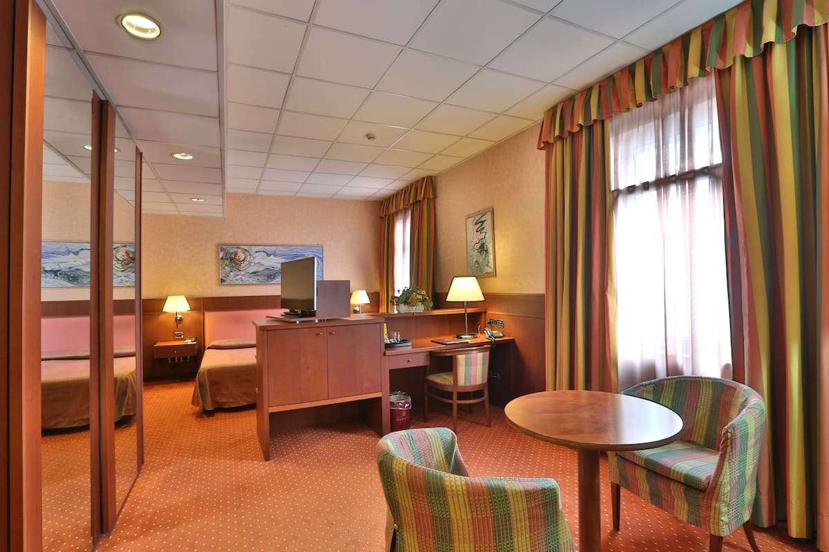 A hotel room with a bed, desk, chair, and a small table.