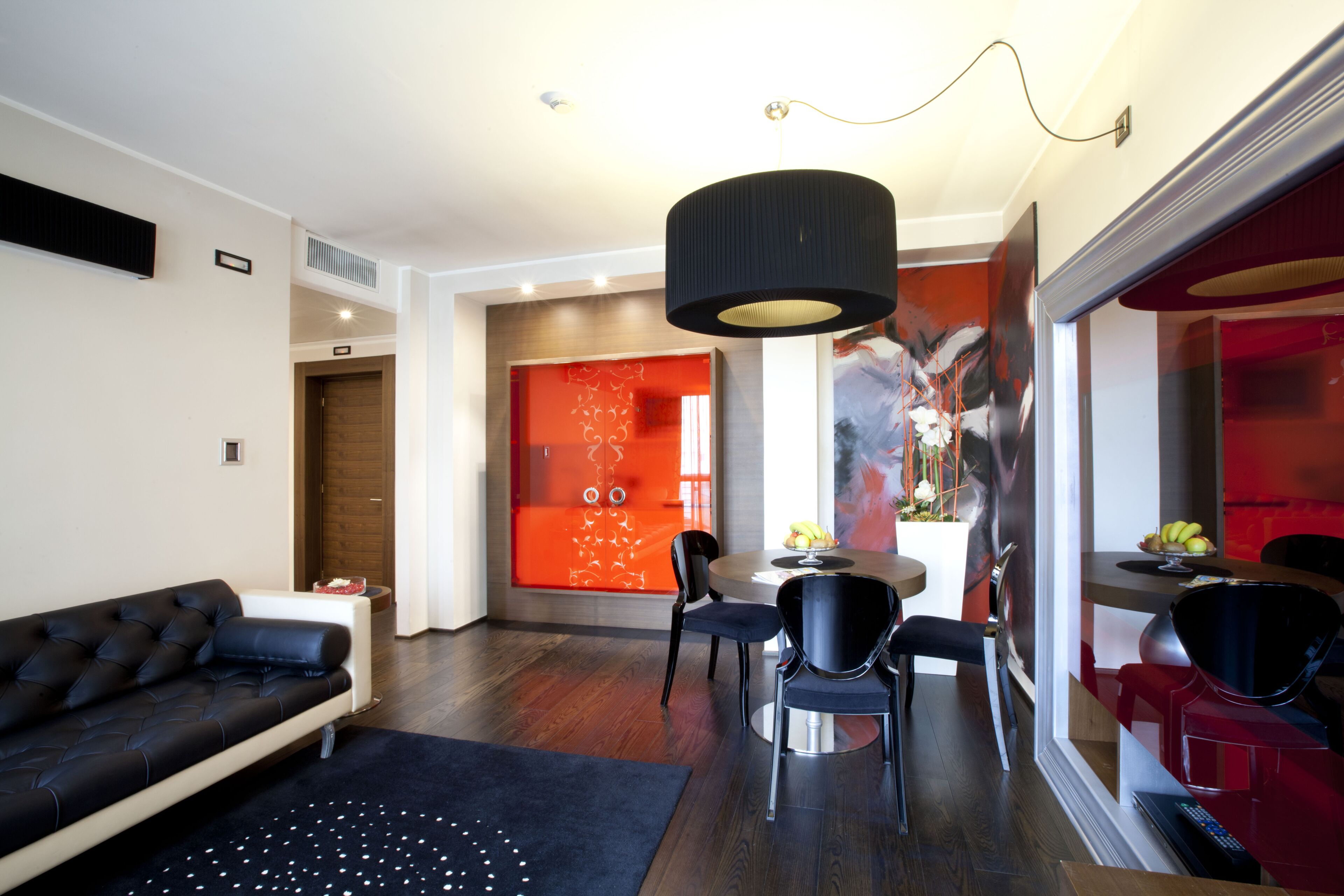 Een moderne woonkamer met een zwarte bank, een eettafel met stoelen en een groot schilderij aan de muur.