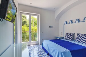 Un dormitorio con cama, televisión montada en la pared, ventana y puerta que da a un balcón.