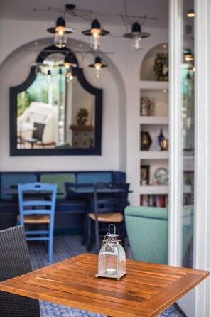 A wooden table with a glass lantern, a blue chair, and a bench in a room with a mirrored wall and shelves. - Mignon Meublè (Sorrento)