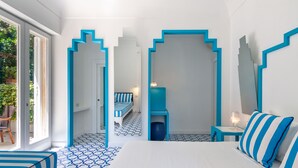 A modern hotel room with a large bed, a seating area with a striped bench, and a view of the outdoors through a glass door. - Mignon Meublè (Sorrento)
