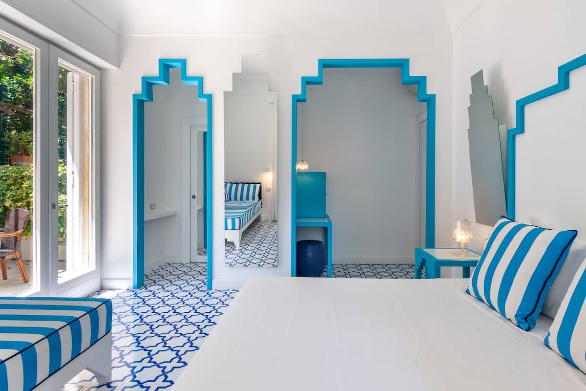 Habitación de hotel moderna con una cama grande, una zona de estar con un banco a rayas y vistas al exterior a través de una puerta de cristal.