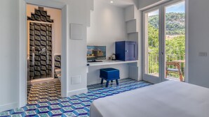 A hotel room with a bed, a small stool, a shelf with a painting, and a view of greenery through a sliding door. - Mignon Meublè (Sorrento)
