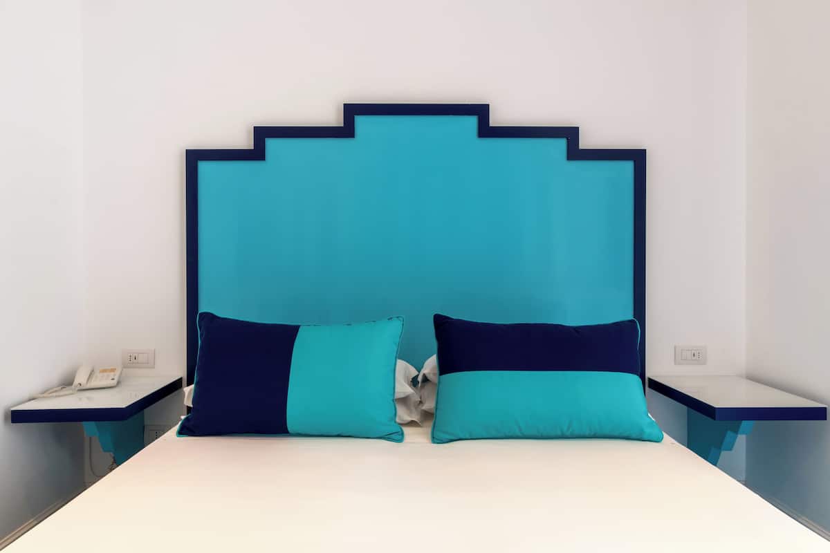 Una cama con cabecera color turquesa, dos almohadas y una mesita de noche con un teléfono.