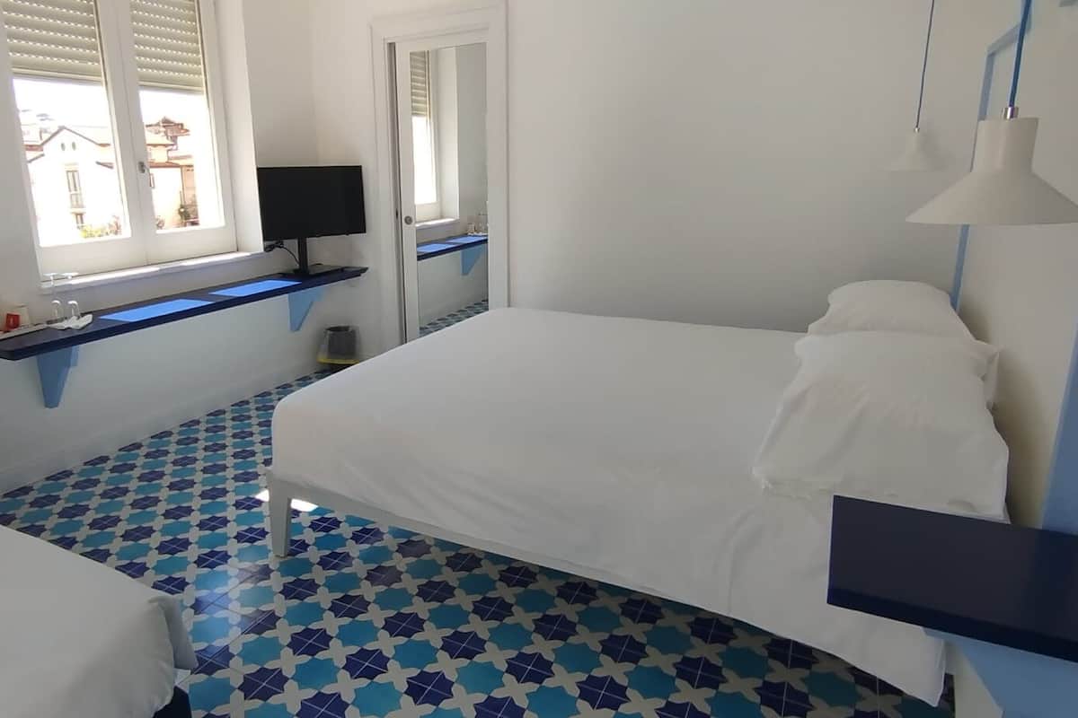 Un dormitorio con cama, escritorio, silla, televisión y ventana con persianas.