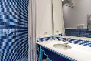 Casa de banho com uma pia branca, azulejos azul e branco quadriculados, chuveiro e espelho.