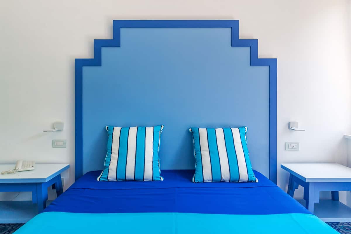 Una habitación con una cama, dos mesitas de noche y un teléfono en la pared.