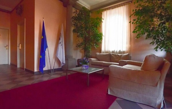 A hotel lobby with a red carpet, beige sofas, a coffee table, and two flags on the wall.