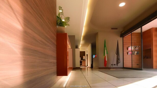 Corredor moderno de hotel com painel de madeira decorativo, uma planta em vaso e uma área de recepção com bandeiras.
