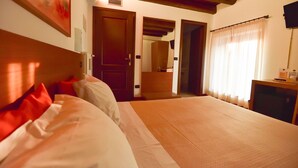 Quarto de hotel com uma cama grande, cabeceira de madeira e uma televisão sobre uma escrivaninha.