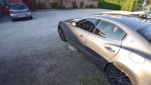 Uma área de estacionamento com dois carros, um prateado e outro bege, estacionados sobre um piso de cascalho.