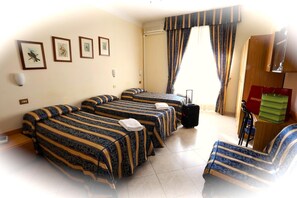 A hotel room with four beds, a desk, a chair, a suitcase, and a window with curtains. - Hotel Loreto (Milan)