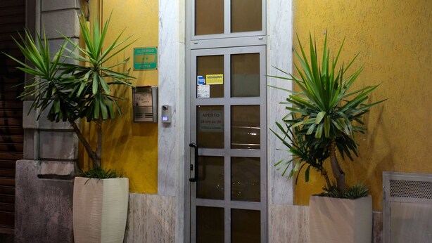 A hotel entrance with a sign reading "HOTEL LORETO" and a star symbol. There are two large potted plants in front of the entrance. - Hotel Loreto (Milan)