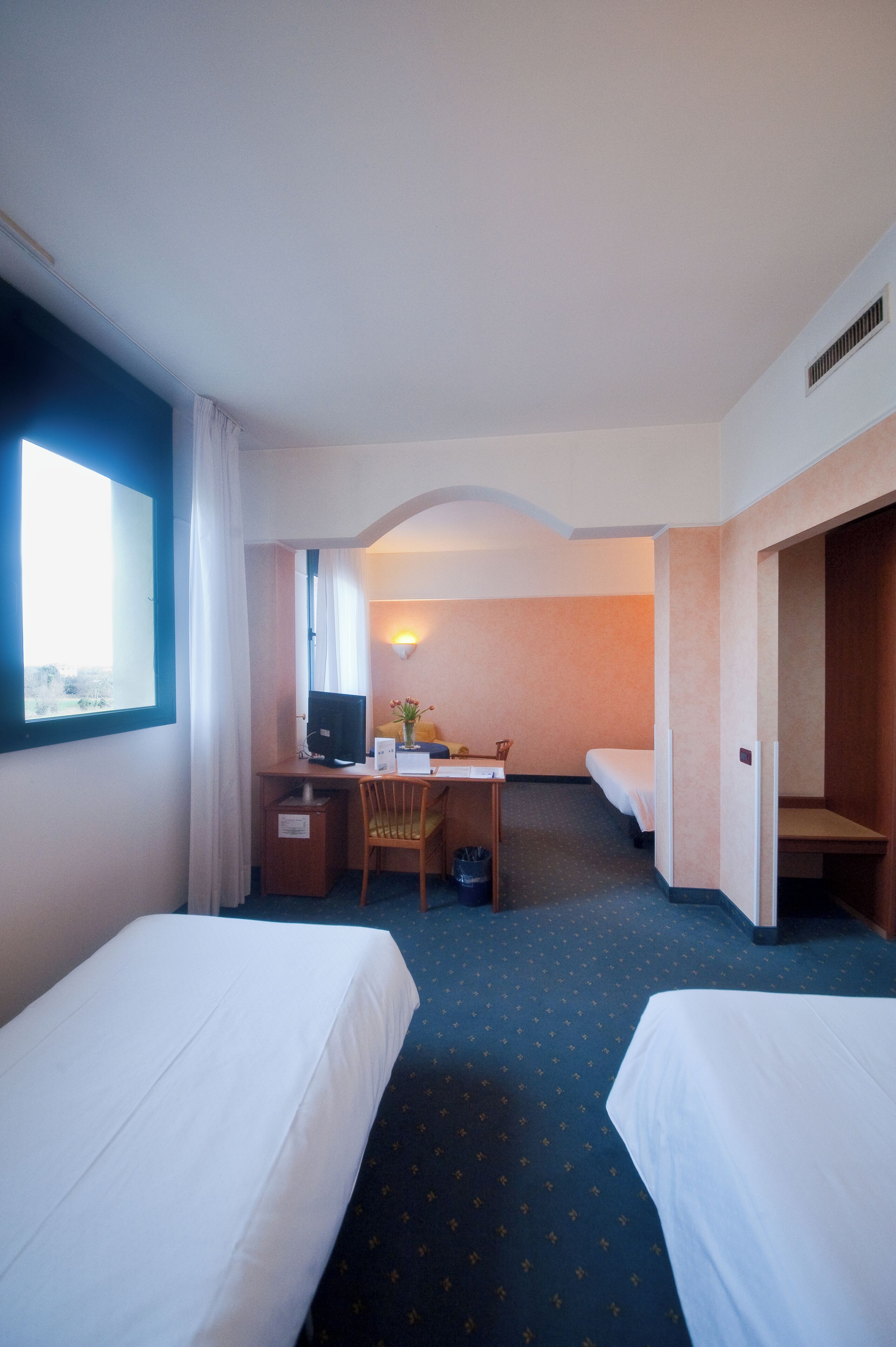A hotel room with two beds, a desk with a computer, a chair, and a small table.