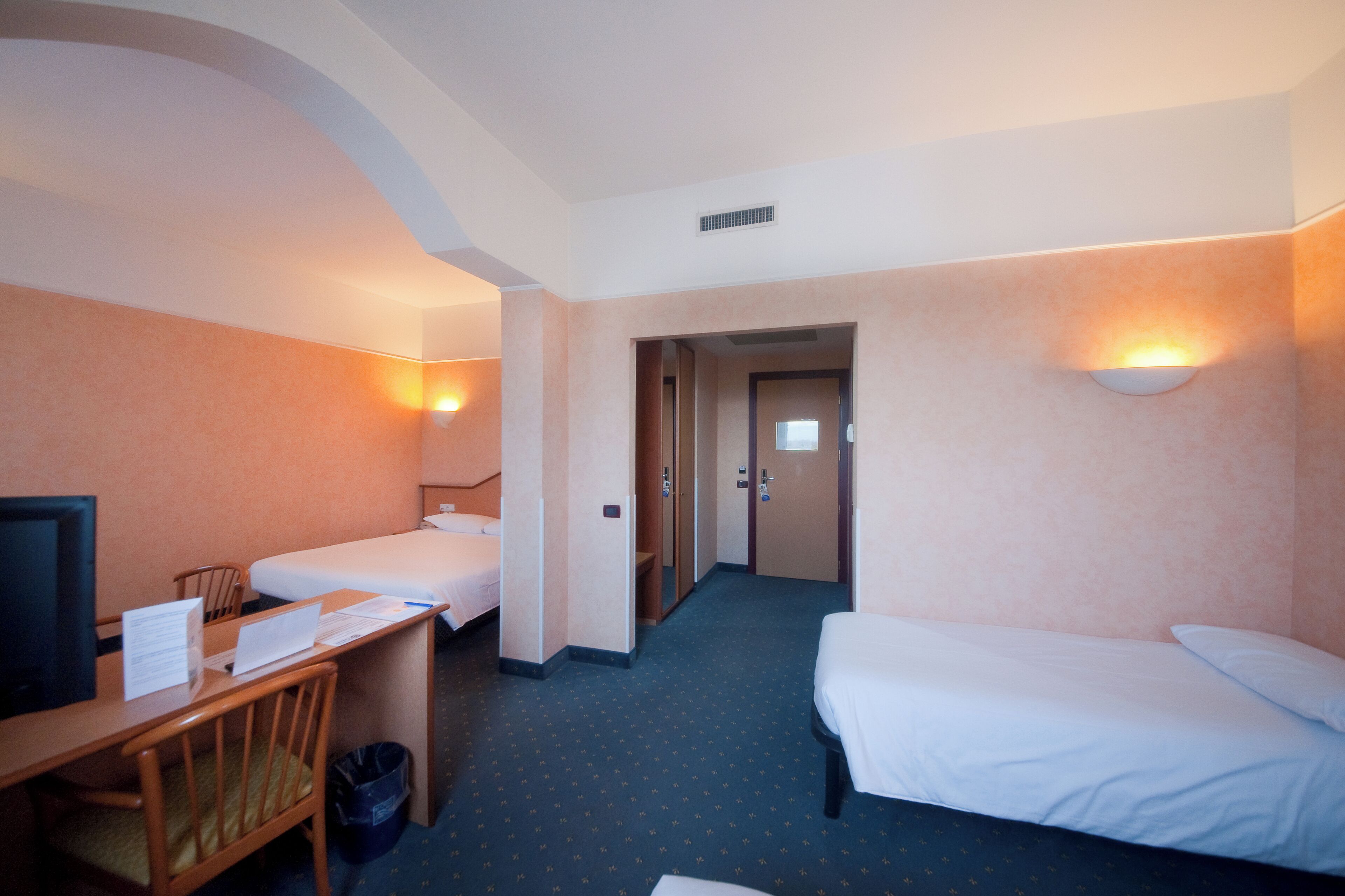 A hotel room with two beds, a desk with a chair, a TV, and a trash bin.