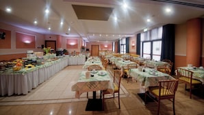 Een ruime eetzaal met meerdere tafels en stoelen, een buffetgedeelte met diverse gerechten, en een plafond met inbouwverlichting.