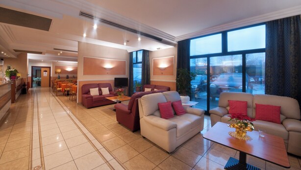Een ruime hotellobby met een modern design, met een mix van zitgedeeltes, een receptiebalie en grote ramen met uitzicht op de parkeerplaats.