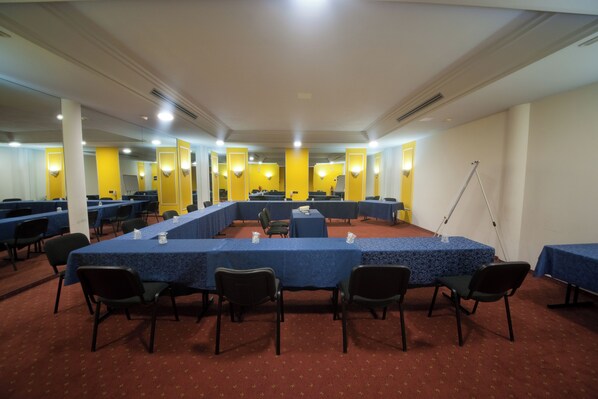 A conference room with multiple tables and chairs, yellow walls, and ceiling lights.