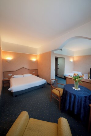 Ein Hotelzimmer mit einem großen Bett, Nachttischen, einem Schreibtisch, einem Stuhl und einem kleinen Tisch mit einer Blumenvase.