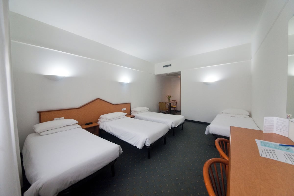 Habitación de hotel con tres camas individuales, un escritorio de madera y una silla.