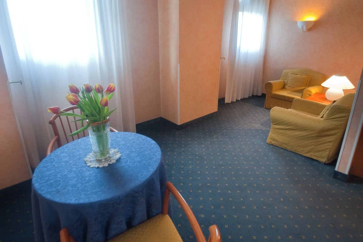 Habitación de hotel con una mesa redonda, una silla, un sofá y una lámpara.
