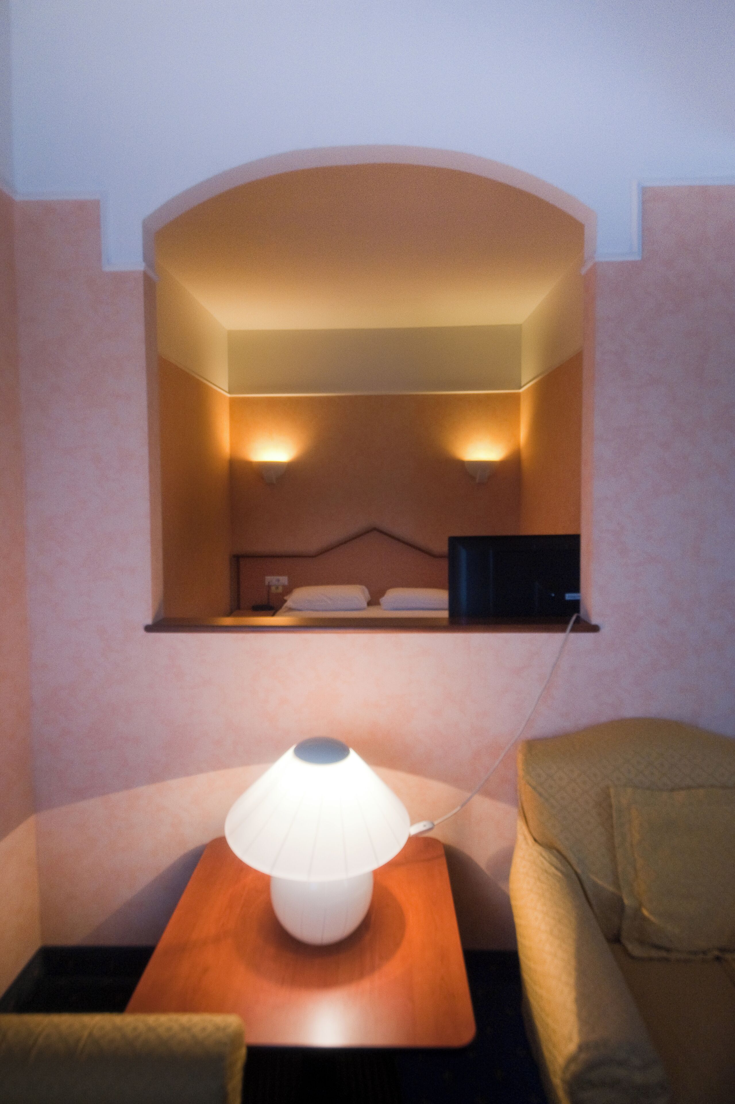A hotel room with a bed, a bedside lamp, a TV, and a small table.
