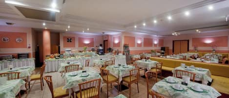 A spacious dining area with multiple tables and chairs, each set with white tablecloths and plates.