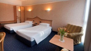 Een hotelkamer met twee eenpersoonsbedden, een nachtkastje met een telefoon, een tafeltje met een bloevas, een bank en een spiegel aan de muur.
