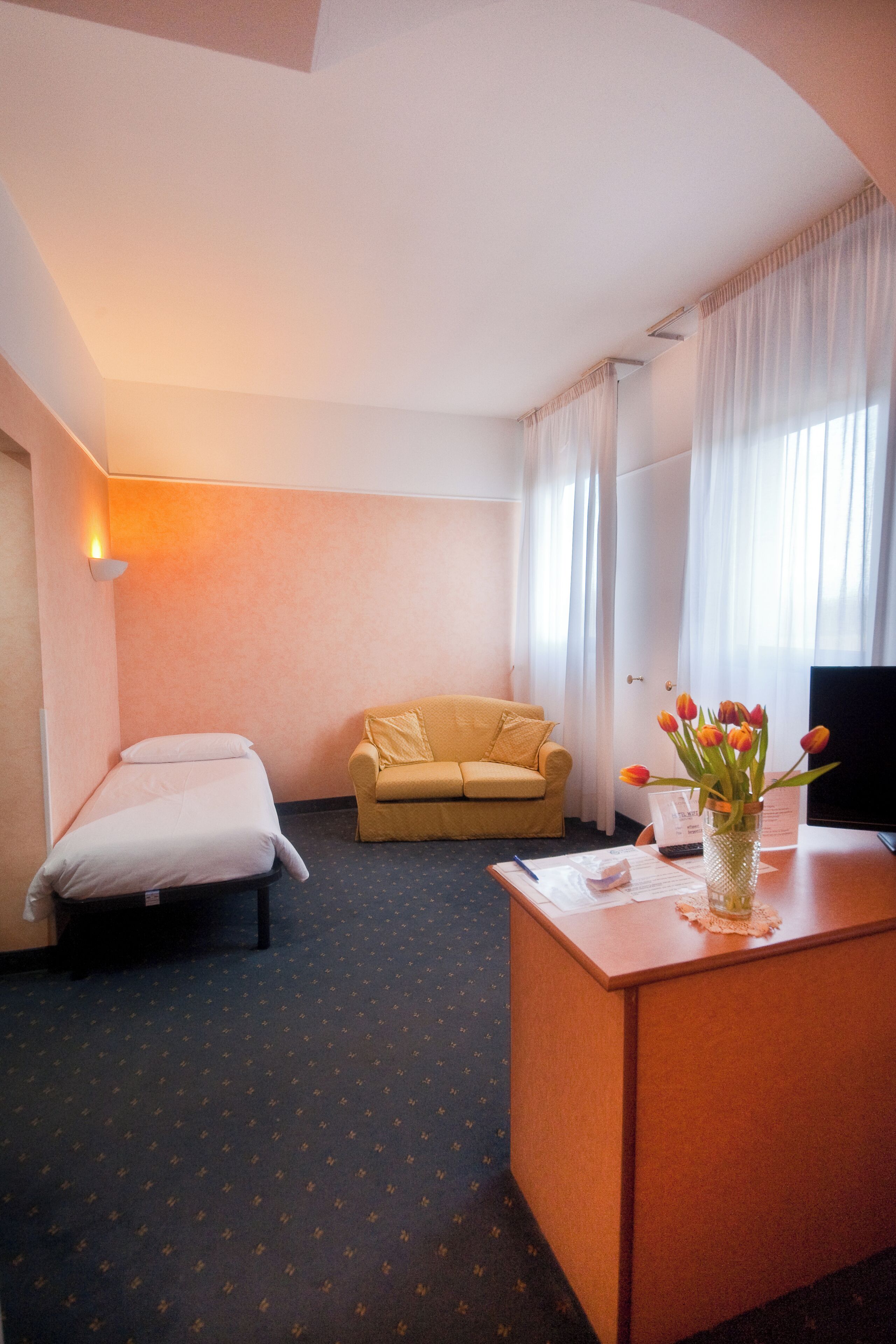 Une chambre d’hôtel avec un lit, un canapé, un bureau agrémenté d’un vase de fleurs et une télévision.