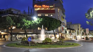 Hotel Tasha, con una fuente en primer plano, rodeado de vegetación y otros edificios.