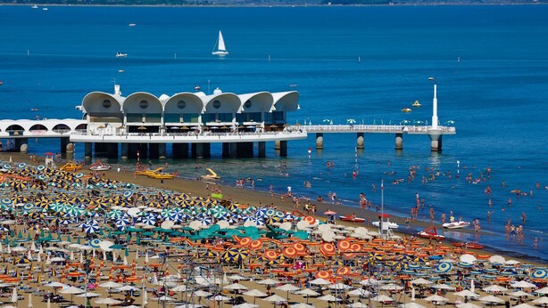 Una playa con numerosos sombrillas de colores y un muelle con un edificio blanco de múltiples arcos.