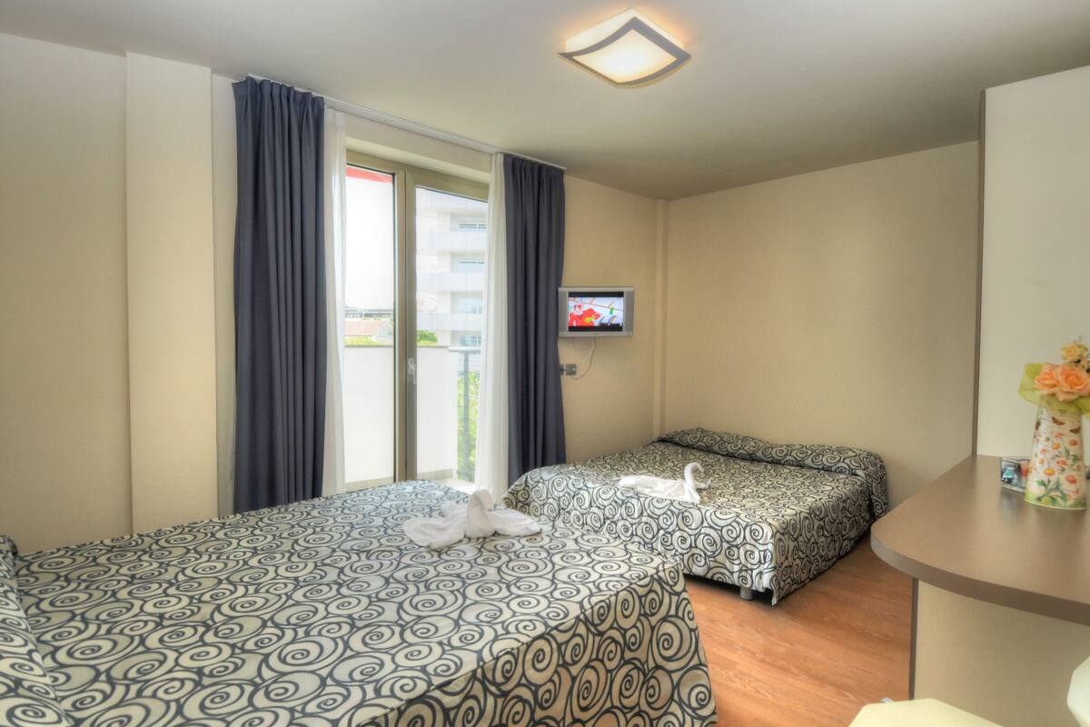 Hotellihuone, jossa on kaksi sänkyä, televisio ja parveke, jossa on verhot.
