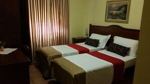 A hotel room with two single beds, a nightstand, a desk, and a window with striped curtains. - Hotel Chopin (Milan)